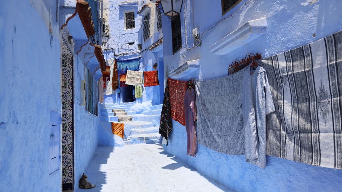 A quiet blue alley in Chefchaouen with textiles hanging on the walls