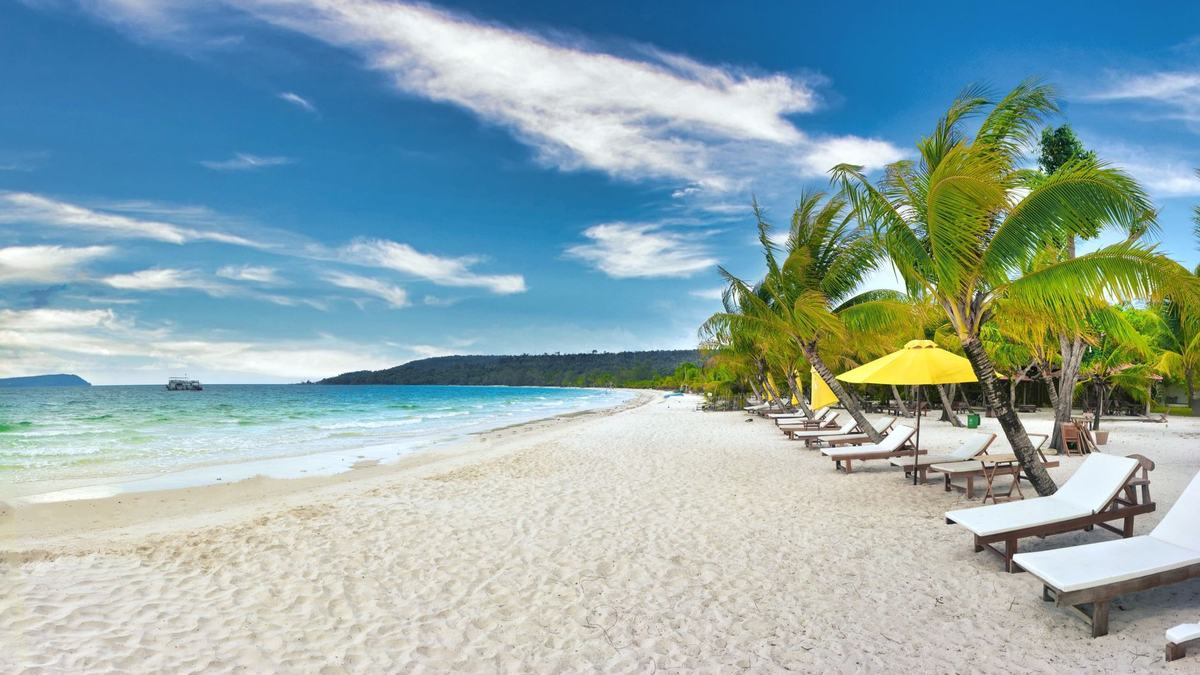 Palm trees and lounge chairs on a white Koh Rong beach under a blue sky