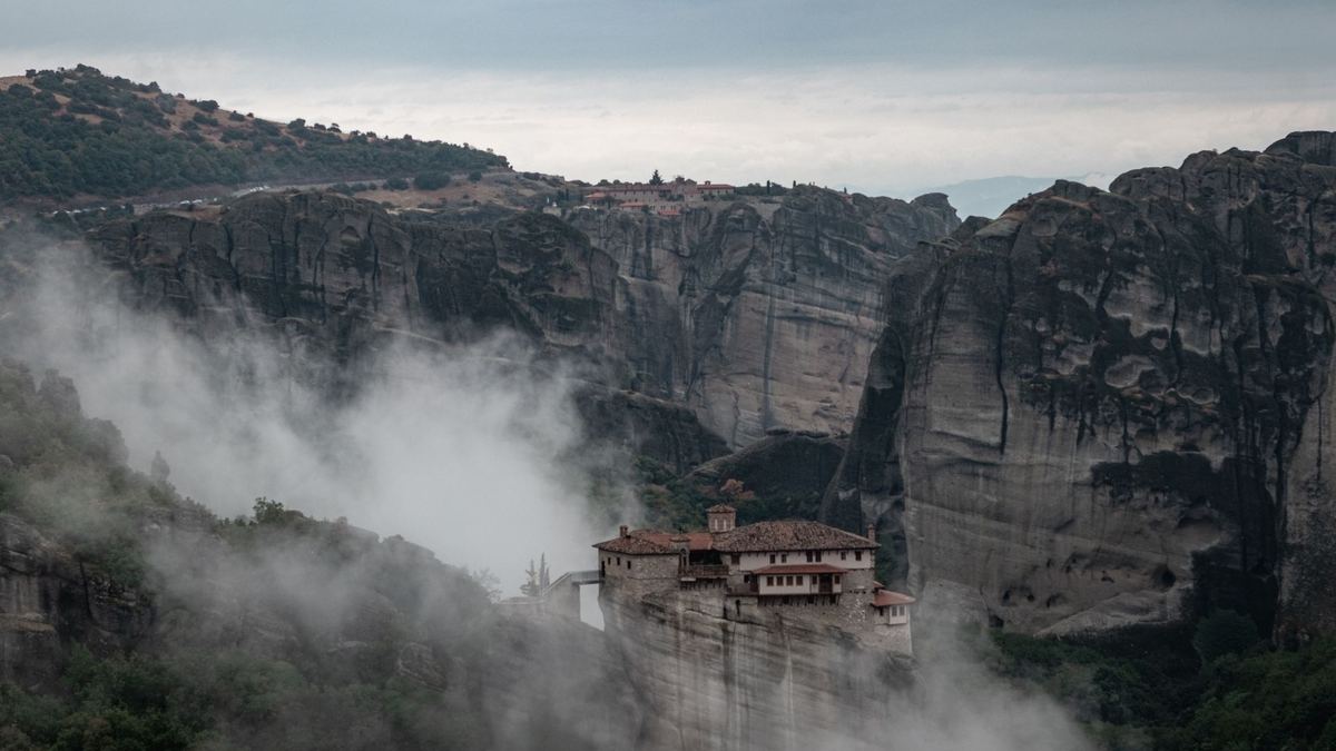 Morning mist rising around a monastery below the Meteora cliffs