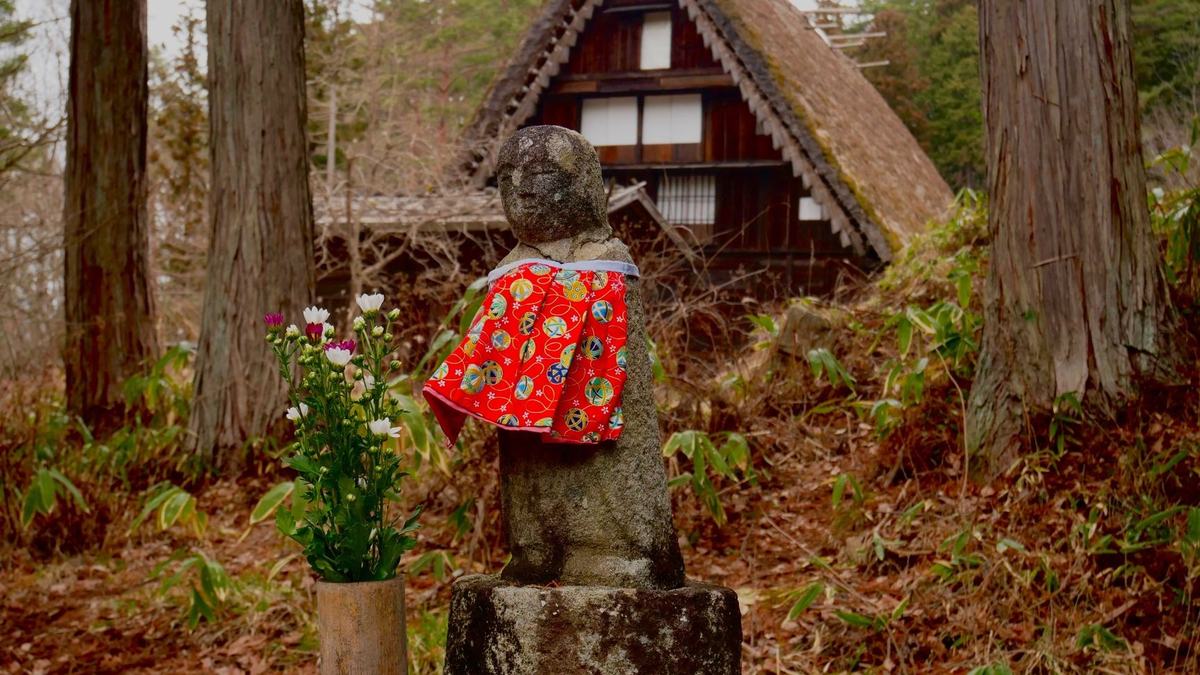 A small stone statue in front of a thatched house
