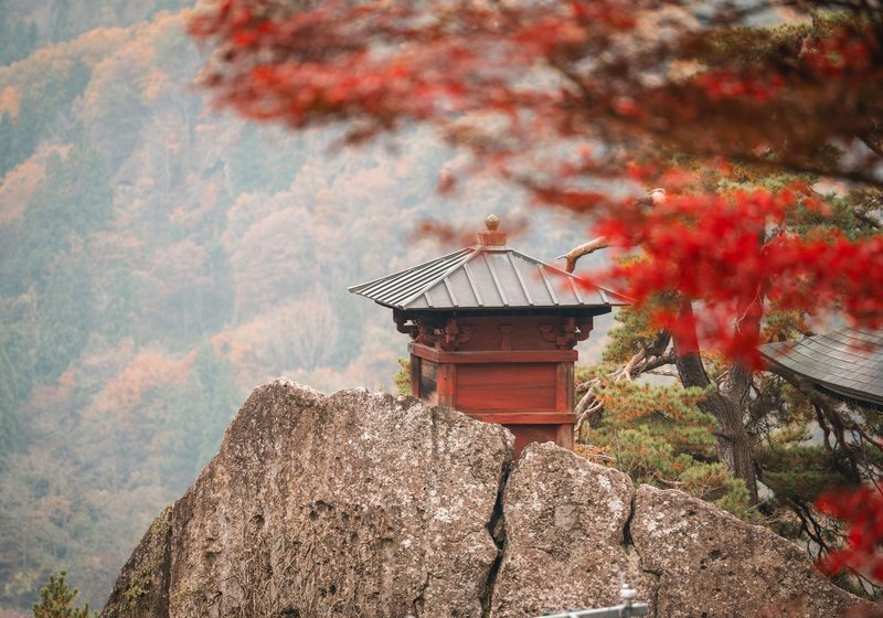 A small red hall on a rock at Yamadera, with autumn leaves